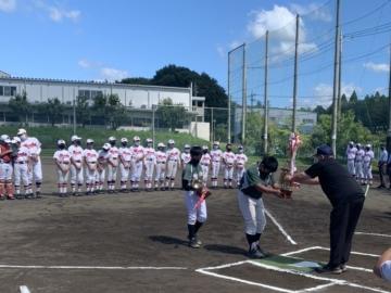 少年野球のチームが見守る中、市長からトロフィーを受け取る緑のユニフォームを着た少年野球の男の子の写真