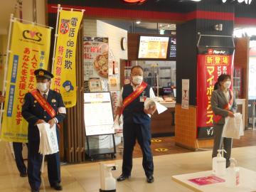 警察官や、市長と女性が、赤いタスキを付けてキャンペーンの品が入った袋を持っている写真