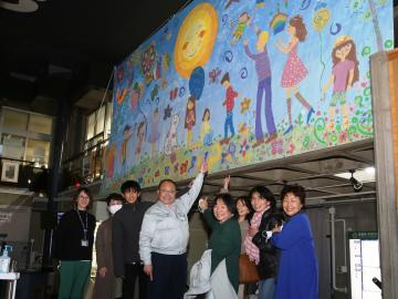 ウクライナの子どもたちが描いた大きな絵の下に笑顔で並んでいる、市長や関係者の写真