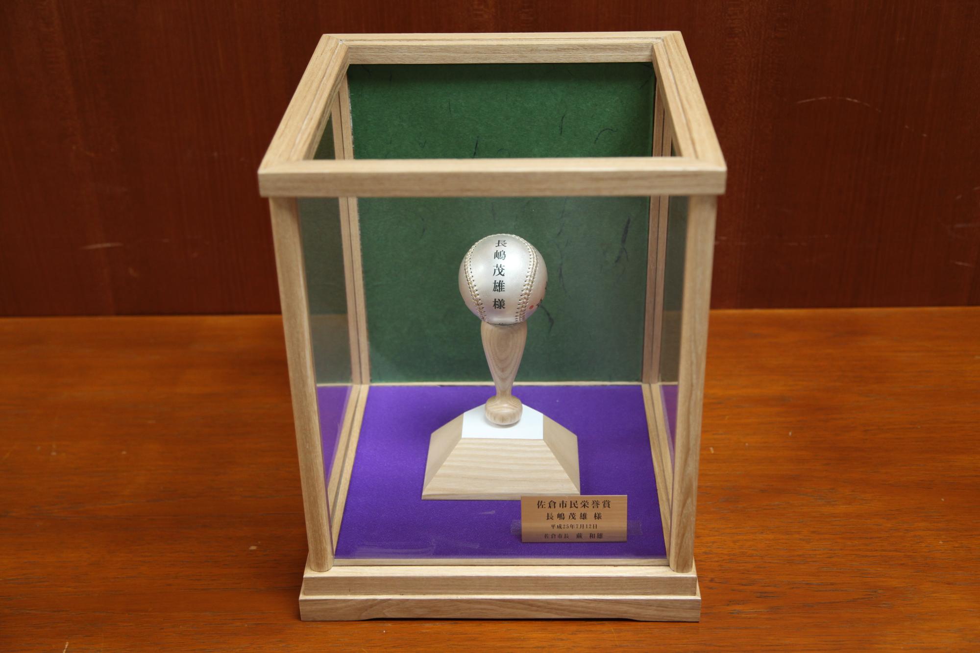 バットの上に銀製の野球ボールがのっている作品がケースに入っている写真
