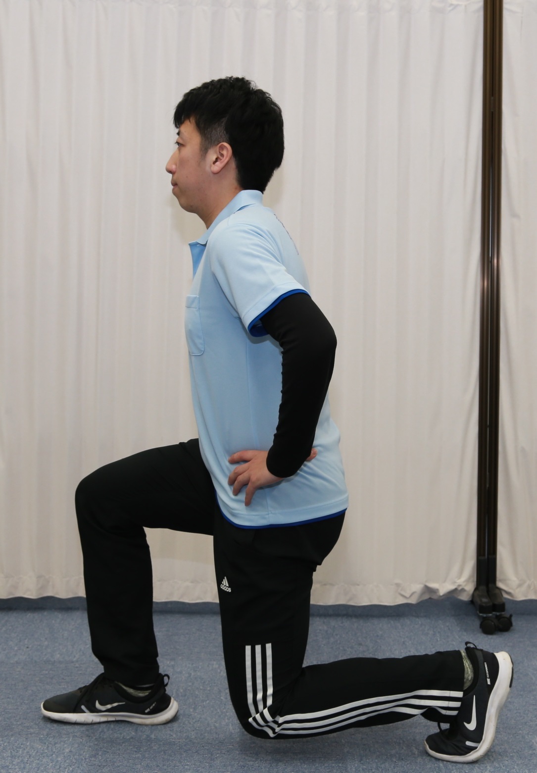 手を腰において片膝立ちのような姿勢のトレーニングをしている男性の写真