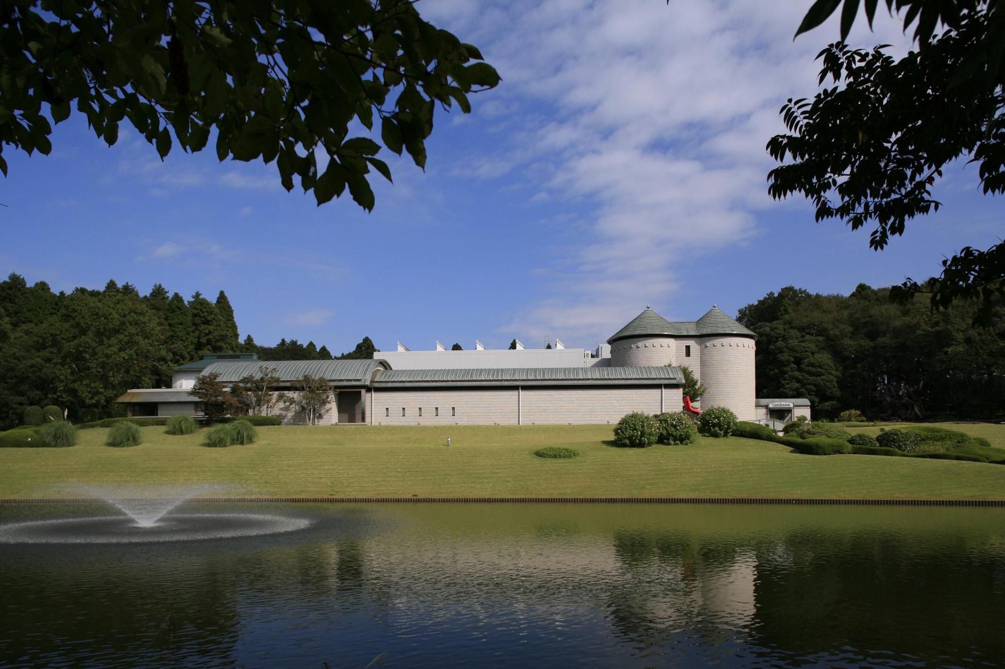 池の向こう側に建つ、白い壁に緑色の屋根のDIC川村記念美術館の外観写真