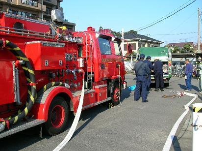 停まっている消防車とごみ収集車の傍に人が集まっている写真