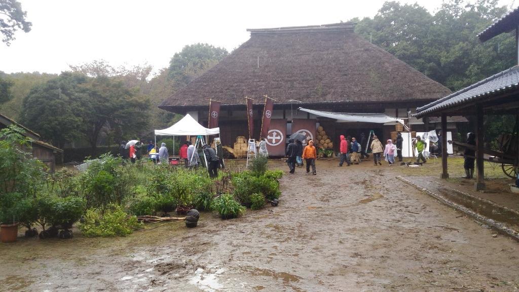 雨の中、茅葺きの屋根 の旧増田家住宅前の庭に、テントや撮影機材が置かれ、スタッフの方が撮影を行っている様子の写真