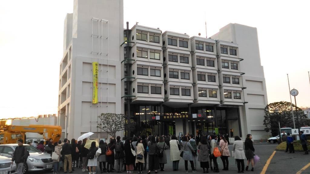 白い外壁の佐倉市役所前で撮影が行われ、沢山の人が見物に集まっている様子の写真
