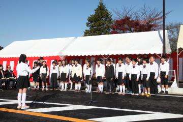 開通された道路に設置されたテントの前で西志津小学校合唱部による合唱が行われている写真