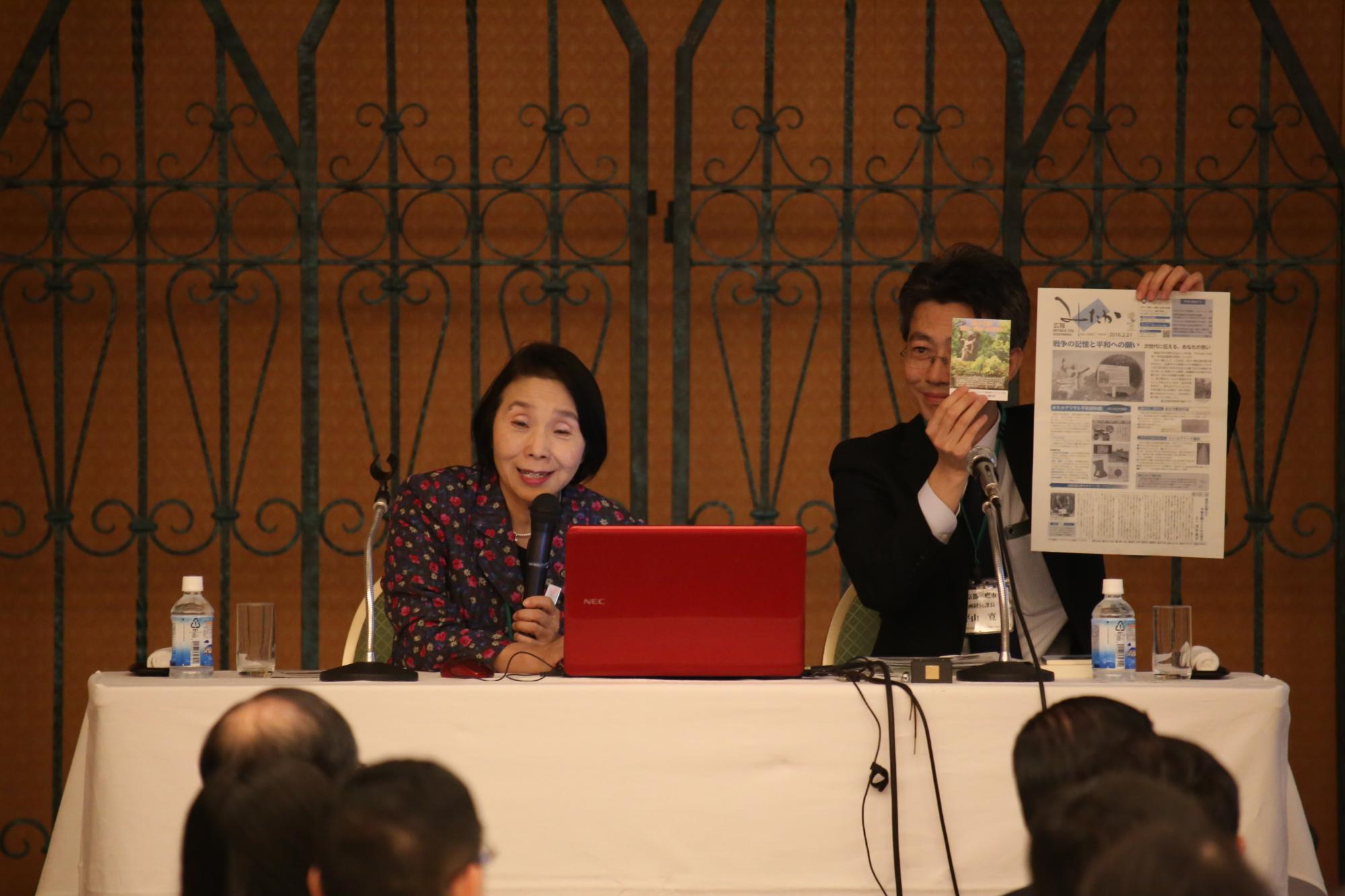 マイクを持って話をする清原慶子三鷹市長と、その横で資料を持っている男性の写真