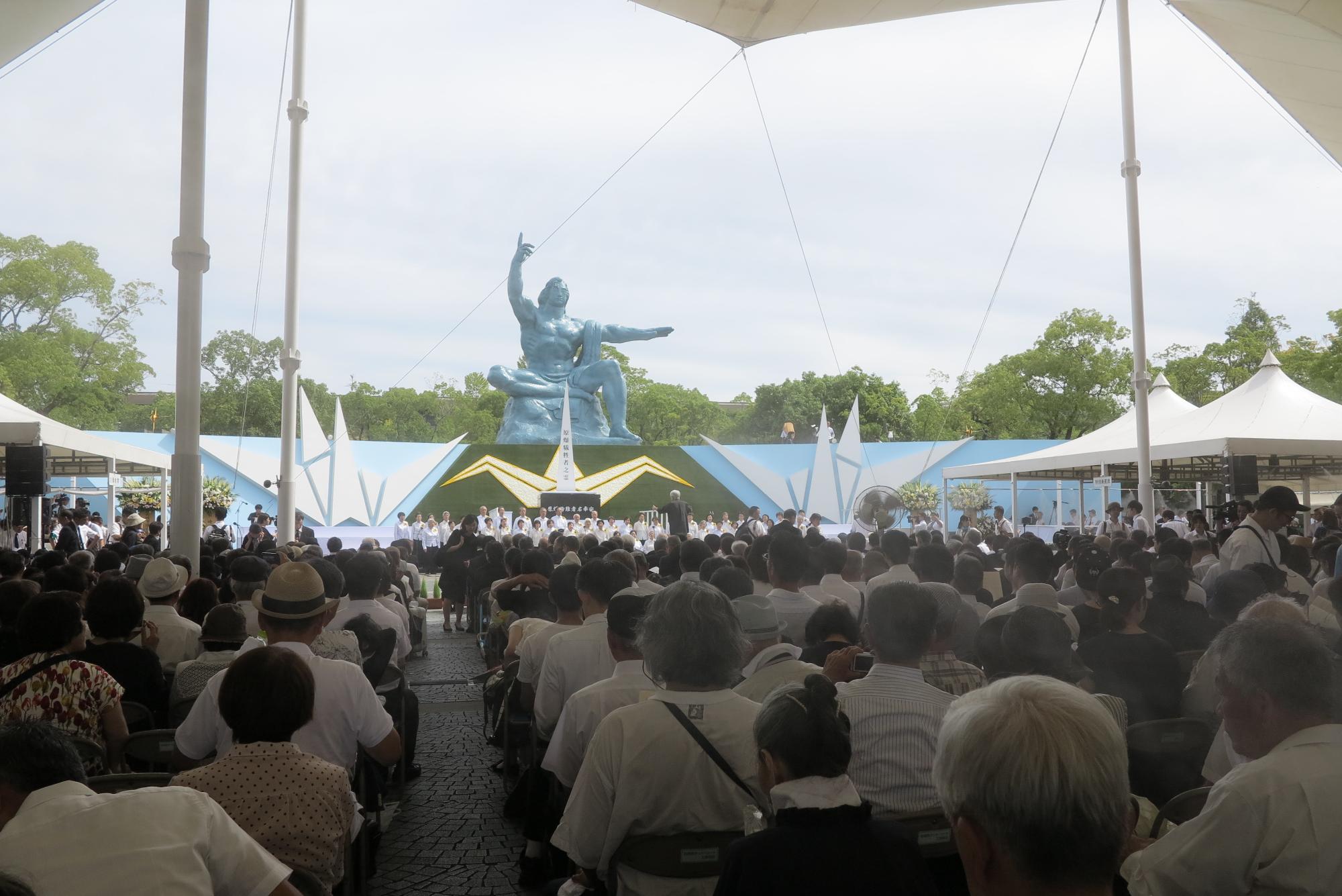 奥に平和祈念像、手前には沢山の式典参加者たちが座っている写真