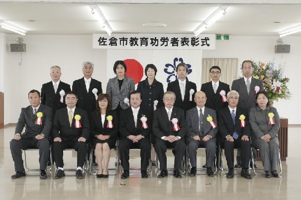 前列に8名、後列に7名の胸章リボンをつけた方々の集合写真