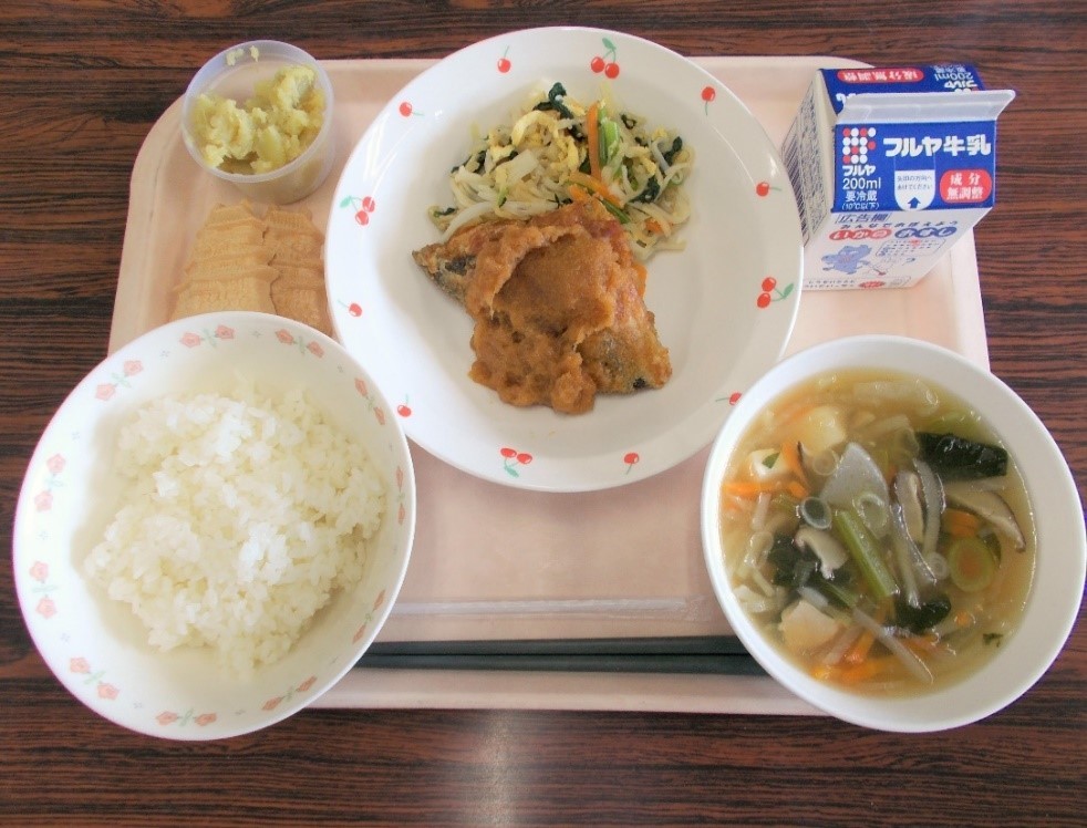 白ご飯、具沢山のスープ、野菜、おかず、牛乳などがお盆に並べられている写真