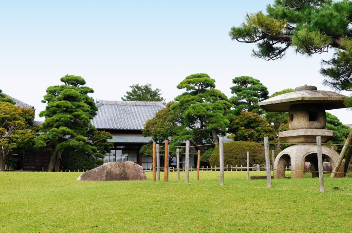 緑の芝生の旧堀田正倫庭園とその奥に建つ旧堀田家住宅を写した写真