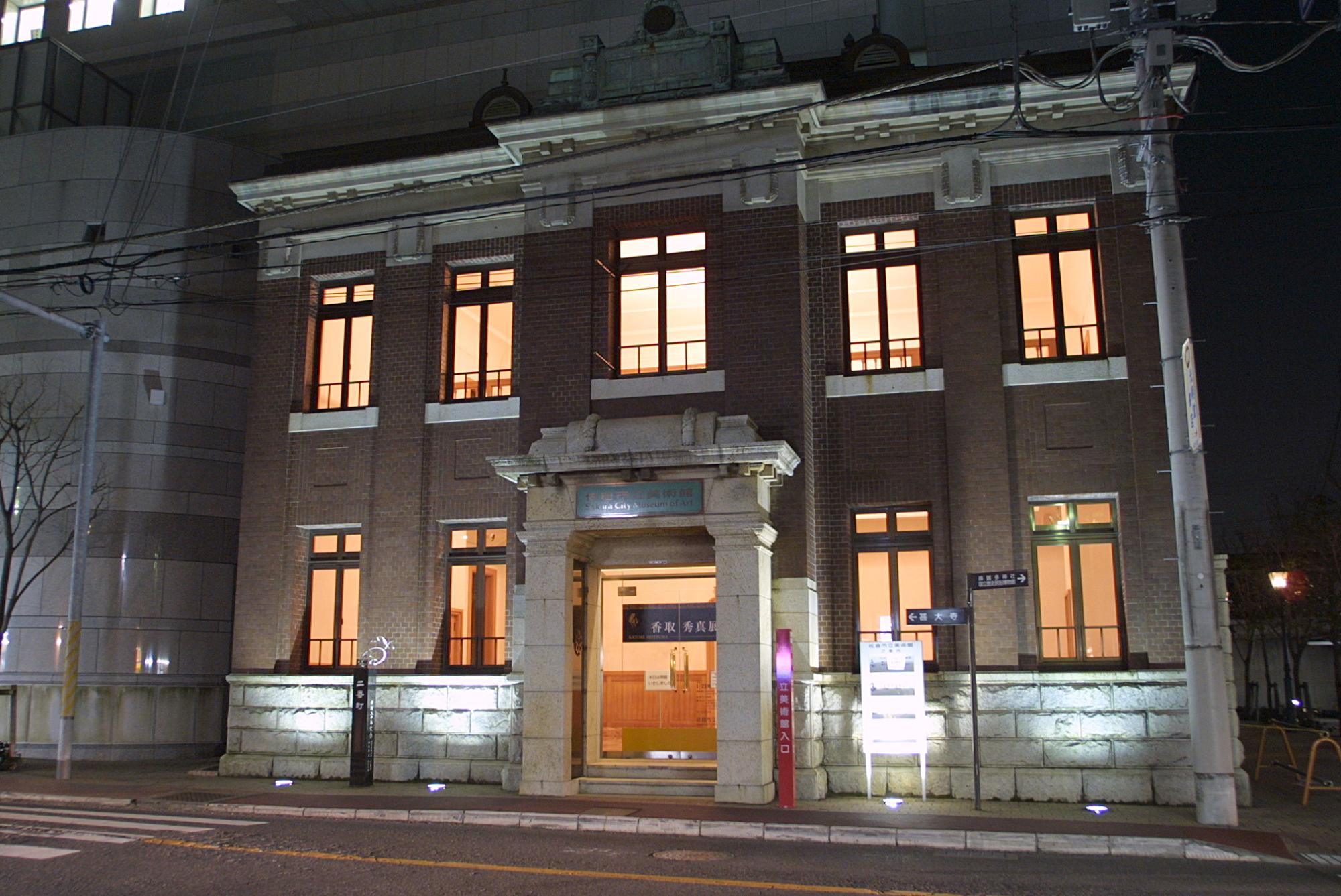 道路沿いに建つ9つの窓と中央の入り口から明かりが見える旧川崎銀行佐倉支店の全体の写真