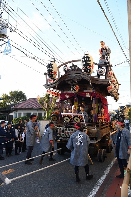 「並木町」と書かれた提灯が飾られた神輿の屋根に1人の男性が立ち、法被姿の参加者が秋祭りの引き廻しをしている写真