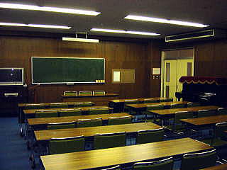 前方に黒板が設置され、右側の壁際にピアノがあり、3人掛けの長机が並んでいる研修室3の写真
