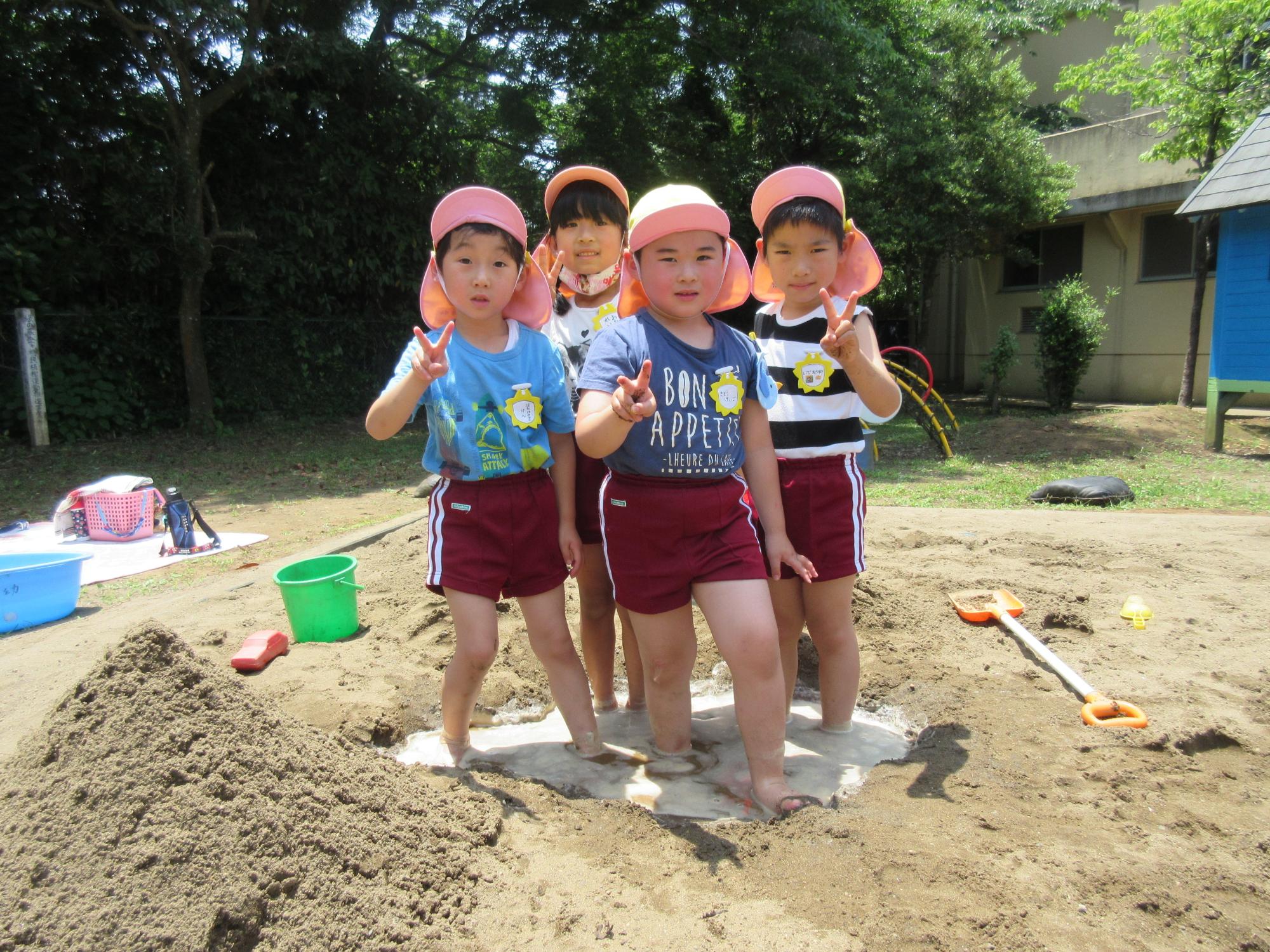 砂場の中に園児4人が立ってピースをしている写真