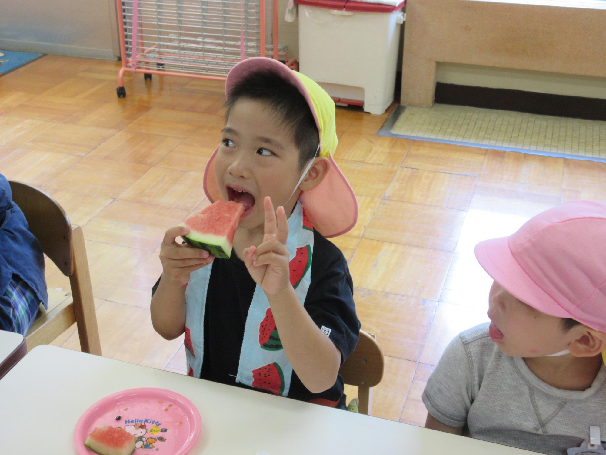 スイカを食べながらピースをしている園児の写真