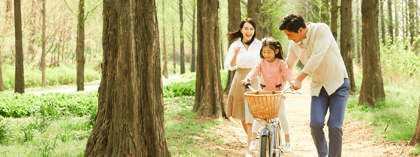 自転車をこぐ女の子とそれを支える父親と笑顔で追いかける母親の画像