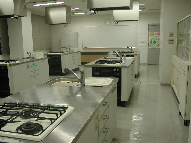 前方にはホワイトボードがあり、ガスコンロと流し台がついている調理台が並んでいる調理室の写真