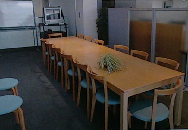 前方にホワイトボードがあり、観葉植物の置かれたテーブルと椅子が設置されている活動コーナーの写真