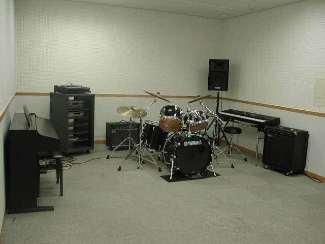 電子ピアノ、ドラムセット、アンプ、シンセサイザーなどが設置されている音楽練習室の写真