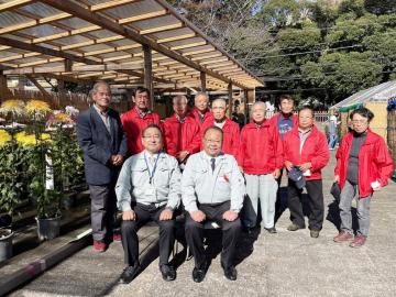 赤いジャケットを着た佐倉市菊花連合会の関係者達と、作業着を着た市長と男性が集まり記念撮影をしている写真