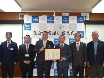 佐倉市感謝状贈呈式にて、額に入った感謝状を持つ市長と男性、その左右に並ぶ関係者達の写真