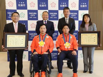 東京2020パラリンピック入賞者 佐倉市表彰式にて、車いすに座った男子選手と椅子に座った男子選手の周りで、額に入った賞状を持つ関係者や、市長が集まっている写真