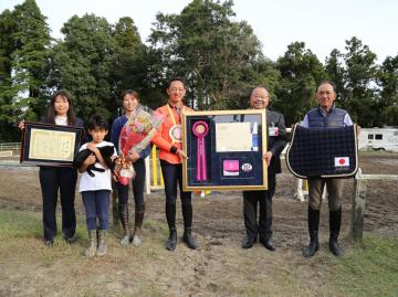 福島大輔選手と市長がメダルや賞状などが入った大きな額を持ち、その左右で家族や関係者が賞状や花束を持って並んでいる写真