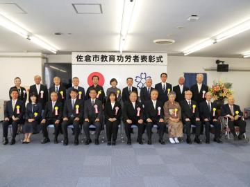 佐倉市教育功労者表彰式にて胸章リボンを付けた関係者が、横2列に並び記念撮影をしている写真