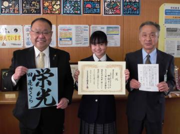 市長、女子学生、男性が書道の作品や賞状を持って並んでいる写真