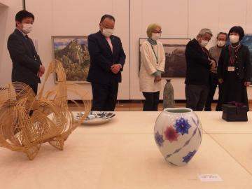 机の上に並べられた工芸品の前に立つ市長や、関係者達の写真