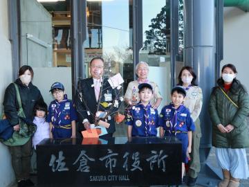 市長とボーイスカウトのメンバーと関係者が、佐倉市役所の石碑の後ろに並び記念撮影をしている写真