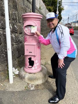 花びらと、黒い猫がデザインされたピンクのポストに、手紙を入れようとしている市長の写真