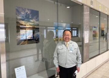 笑顔の市長が、ガラスのショーウインドウの中に飾られた写真の前に立っている写真