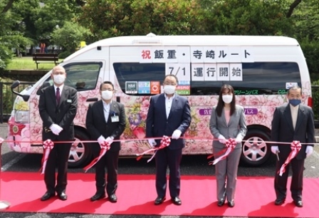 桜がデザインされたバスの前で、市長と4名の関係者が、テープカットのリボンの前に並んでいる写真