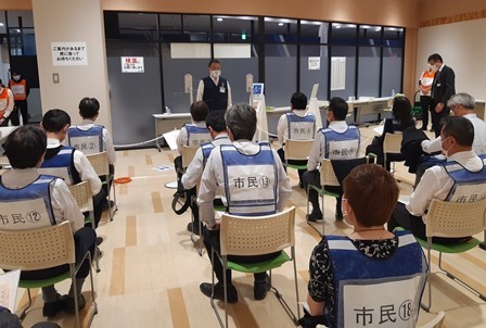 市民と書かれたベストを着て、並べられた椅子に着席している関係者達の写真