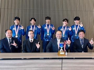 首にメダルをかける箱根駅伝でのチームメンバー5名と、その前に並んで着席する市長や関係者の記念写真
