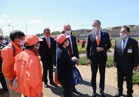 スーツを着た外国人の男性3名と市長が、オレンジ色の帽子を被った関係者の前に立っている写真