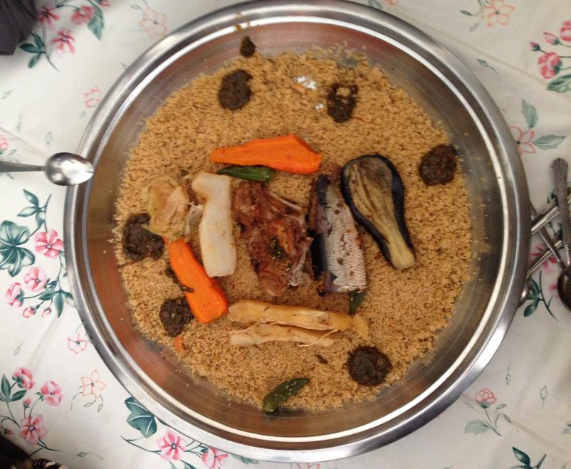 シルバーの丸い器に薄茶色をしたお米、その上に野菜や魚がのっている「チェブ・ジェン」の写真