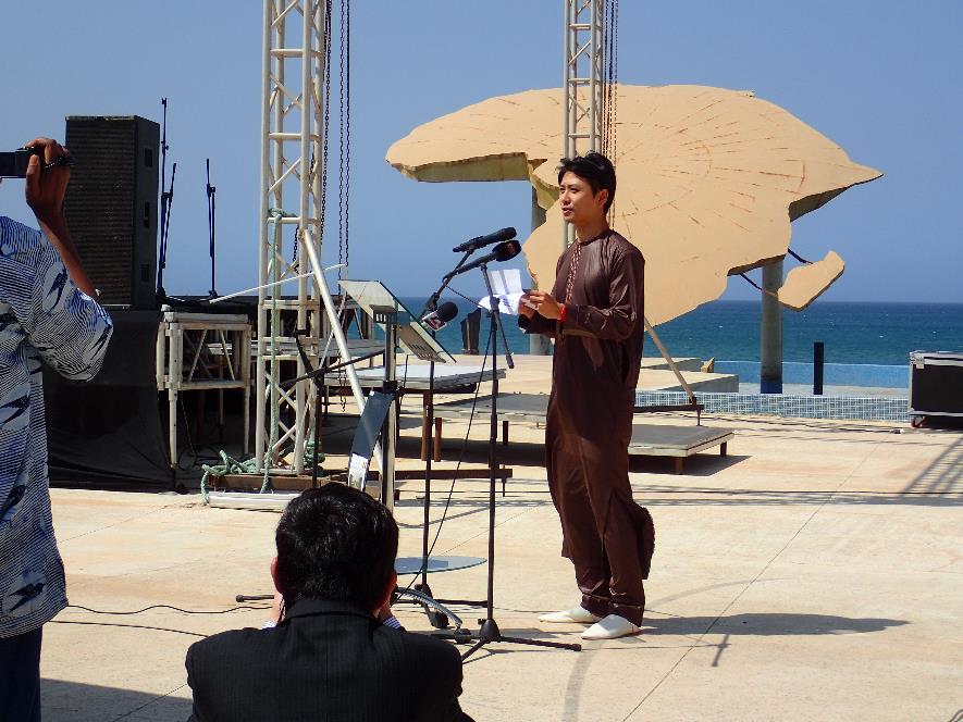 茶色い服を着た原田拓朗さんがマイクの前でスピーチをしている写真