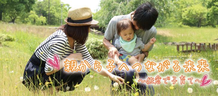 親から子へつながる未来～佐倉で子育て～お父さんが子供を膝に乗せ、お母さんが小さな黄色い花を指差している写真