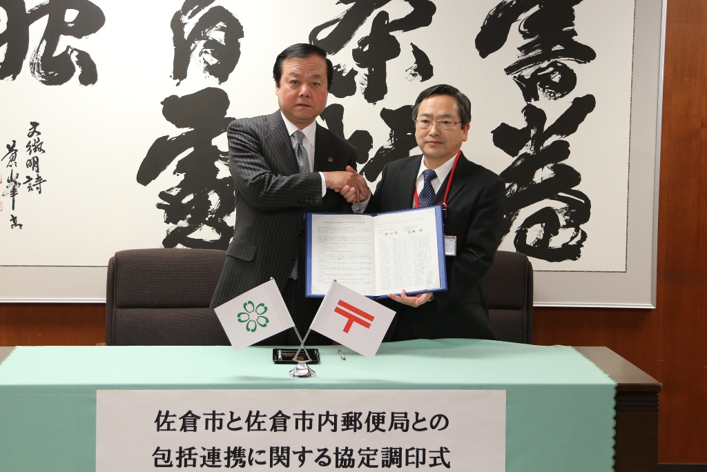 佐倉郵便局 岡野局長が協定書を持ち蕨市長と握手を交わしている写真
