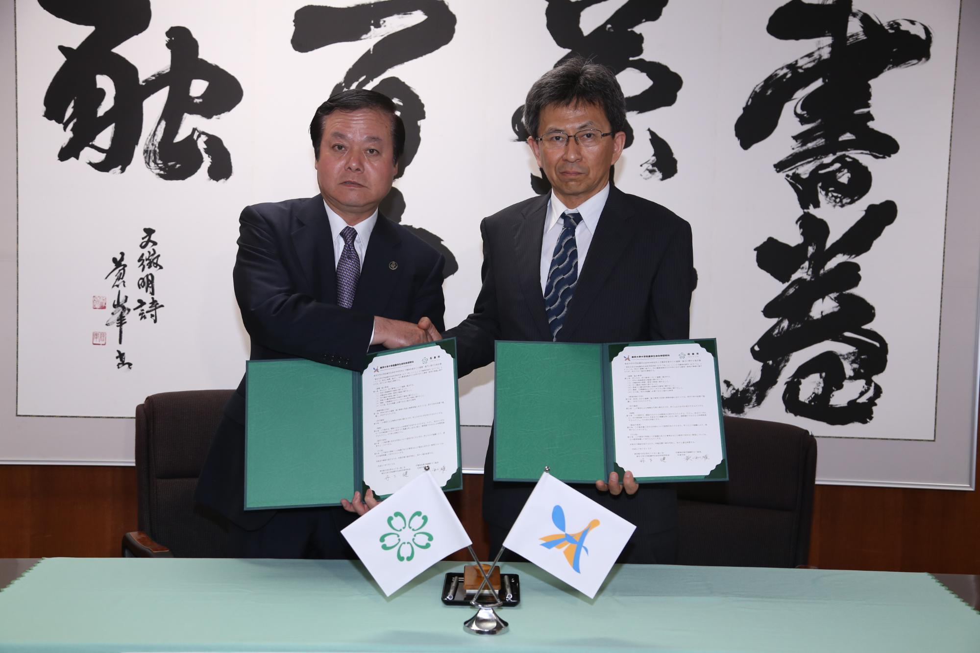 蕨市長と東京大学大学院農学生命科学研究科長 丹下さんがお互いに協定書を持って握手をしている写真