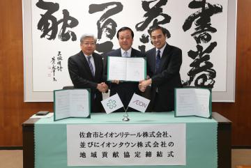 市長が中央で開いた協定書を持ち、左側に岡崎 双一 代表取締役社長、右側に大門 淳 代表取締役社長が立ちそれぞれが握手を交わしている写真