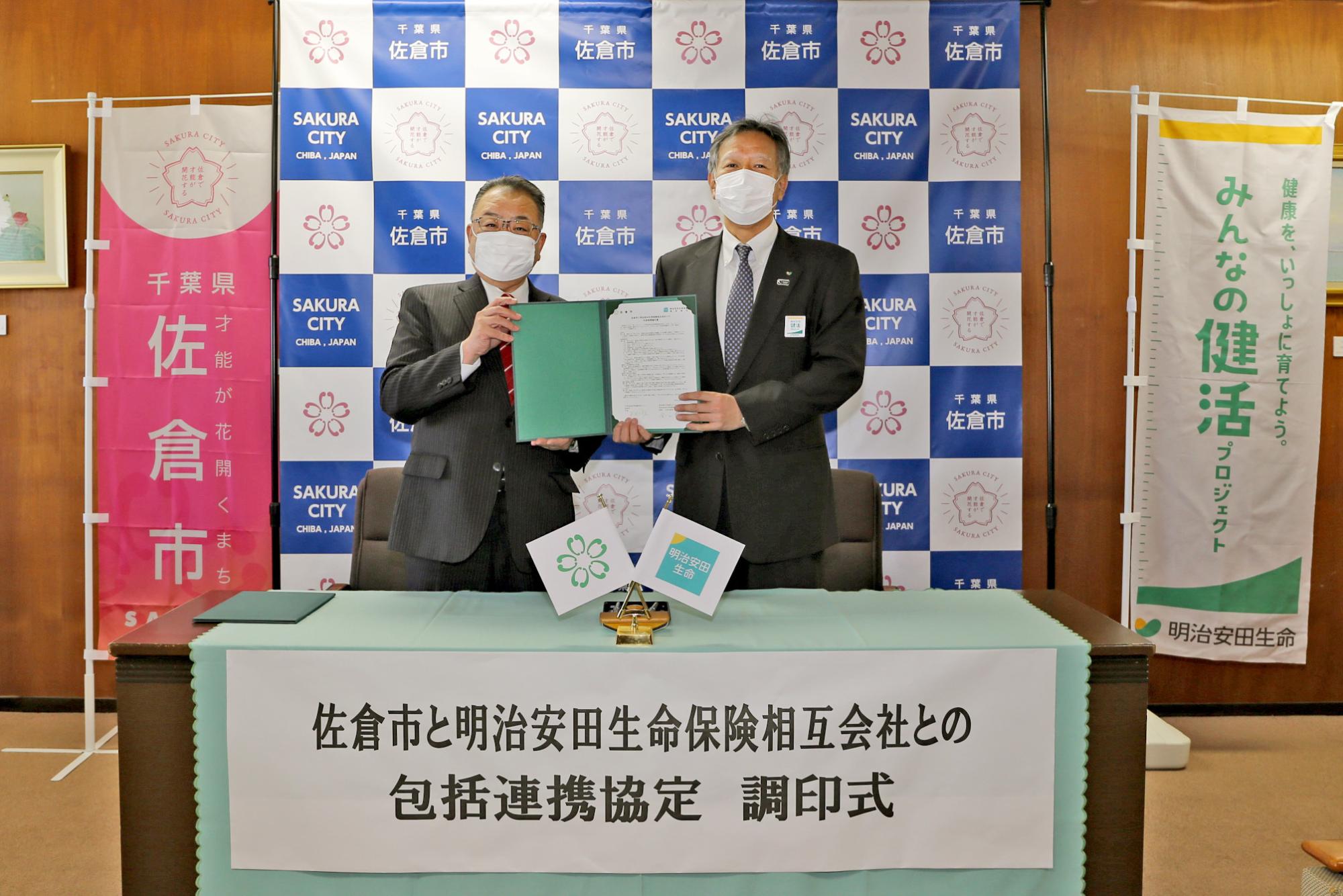 調停式にてマスク姿の西田市長と明治安田生命保険相互会社 金山本部長が一緒に協定書を手に持っている写真