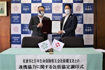 黒いホルダーに協定書があり、そのホルダーを西田市長と日本生命相互会社 中山支店長が一緒に持っている写真