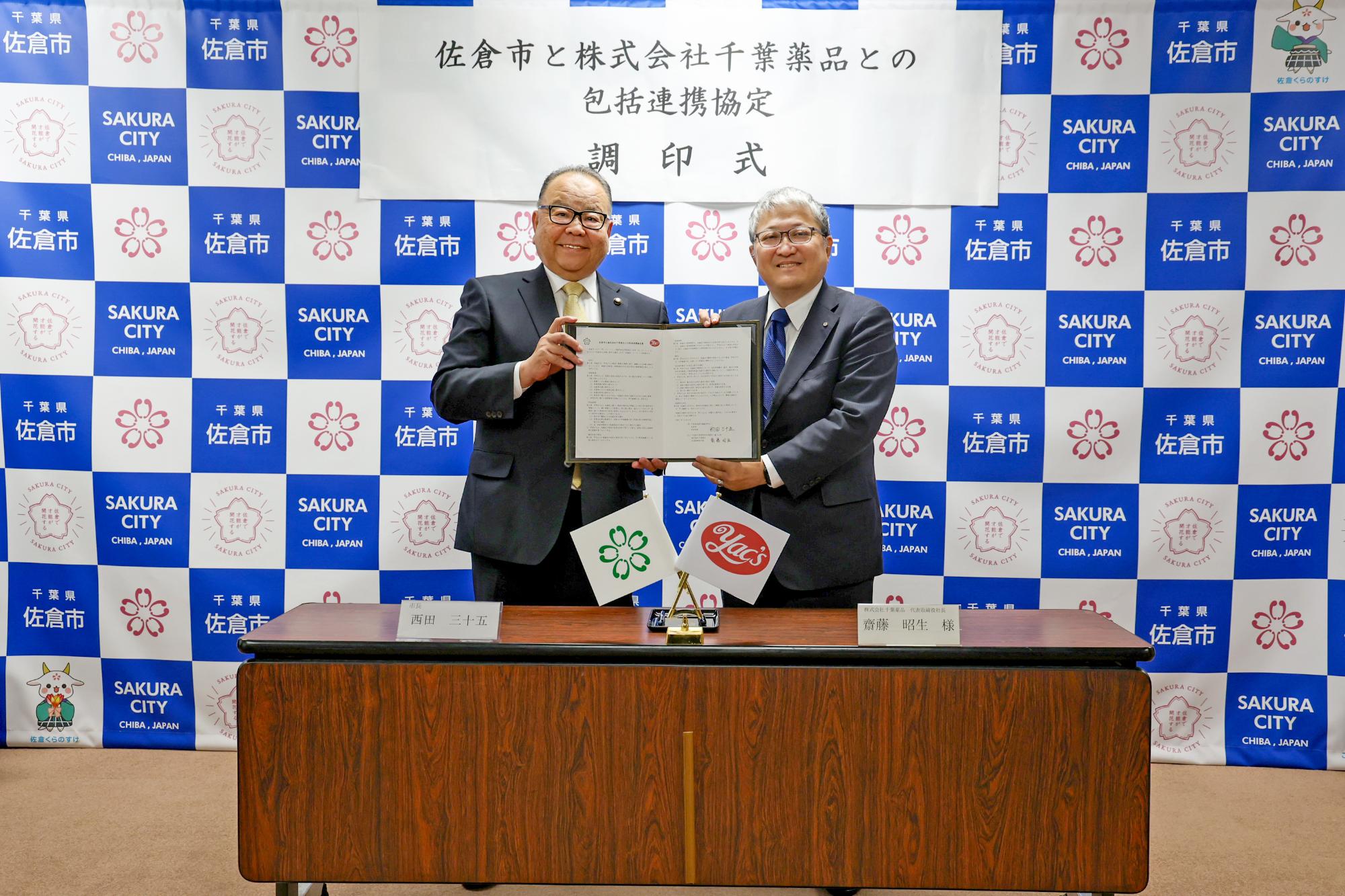 写真：署名済の協定書を掲げる西田三十五佐倉市長（左）、齋藤昭生代表取締役社長（右）