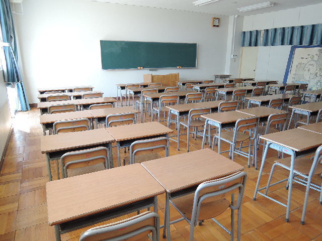 奥に黒板があり、机と椅子がセットになって設置されている学習室を後方から撮影した写真