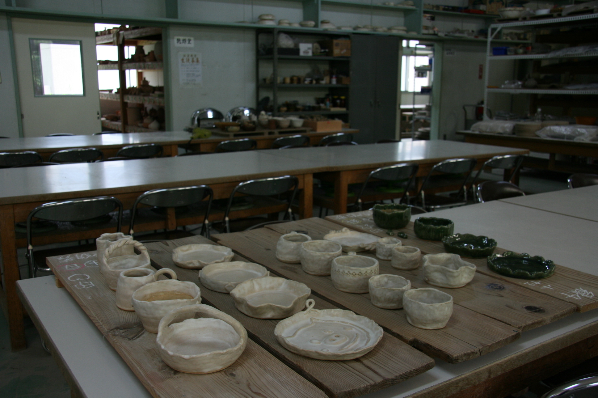 陶芸教室の大きな作業台の上に5つの細長い板が乗せられ、陶芸作品が並んで置いてある写真