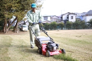 芝刈り機を使ってグラウンドの芝を刈っている職員の写真